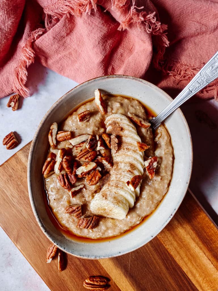 bowl of porridge oats, topped with banana, cinnamon, pecans and maple syrup