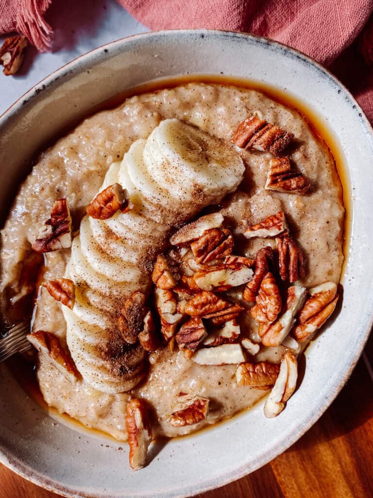 bowl of oats, topped with banana, cinnamon, maple syrup and pecans